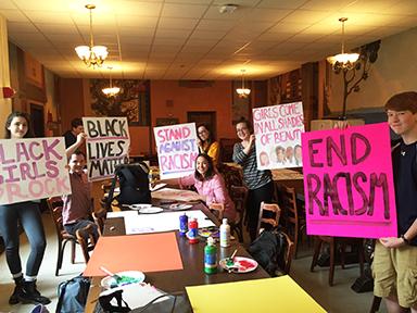 Students hold up posters made during an after school poster party. Each sign promoting racial equality in school and in our community.