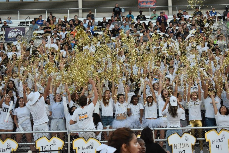 The student section throws gold strands into the air at kickoff. 