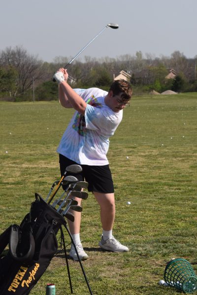 Captain Brock Rogers prepares to strike the ball into a field of scattered golf balls hit by others.
